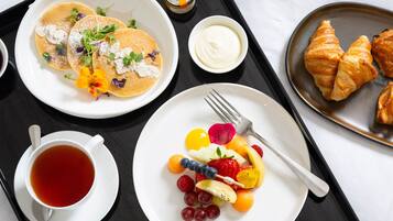Bandeja de desayuno con panqueques, cruasanes, fruta y una taza de té.
