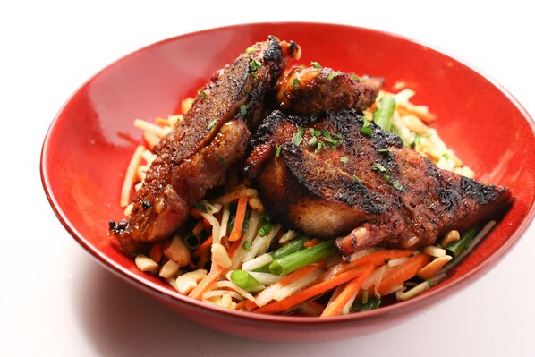 A red bowl containing grilled meat and a vegetable salad.