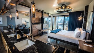 A modern hotel room with a large bed, a separate bathroom with a sink, and a city view through large windows.