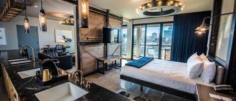 A modern hotel room with a large bed, a separate bathroom with a sink, and a city view through large windows.
