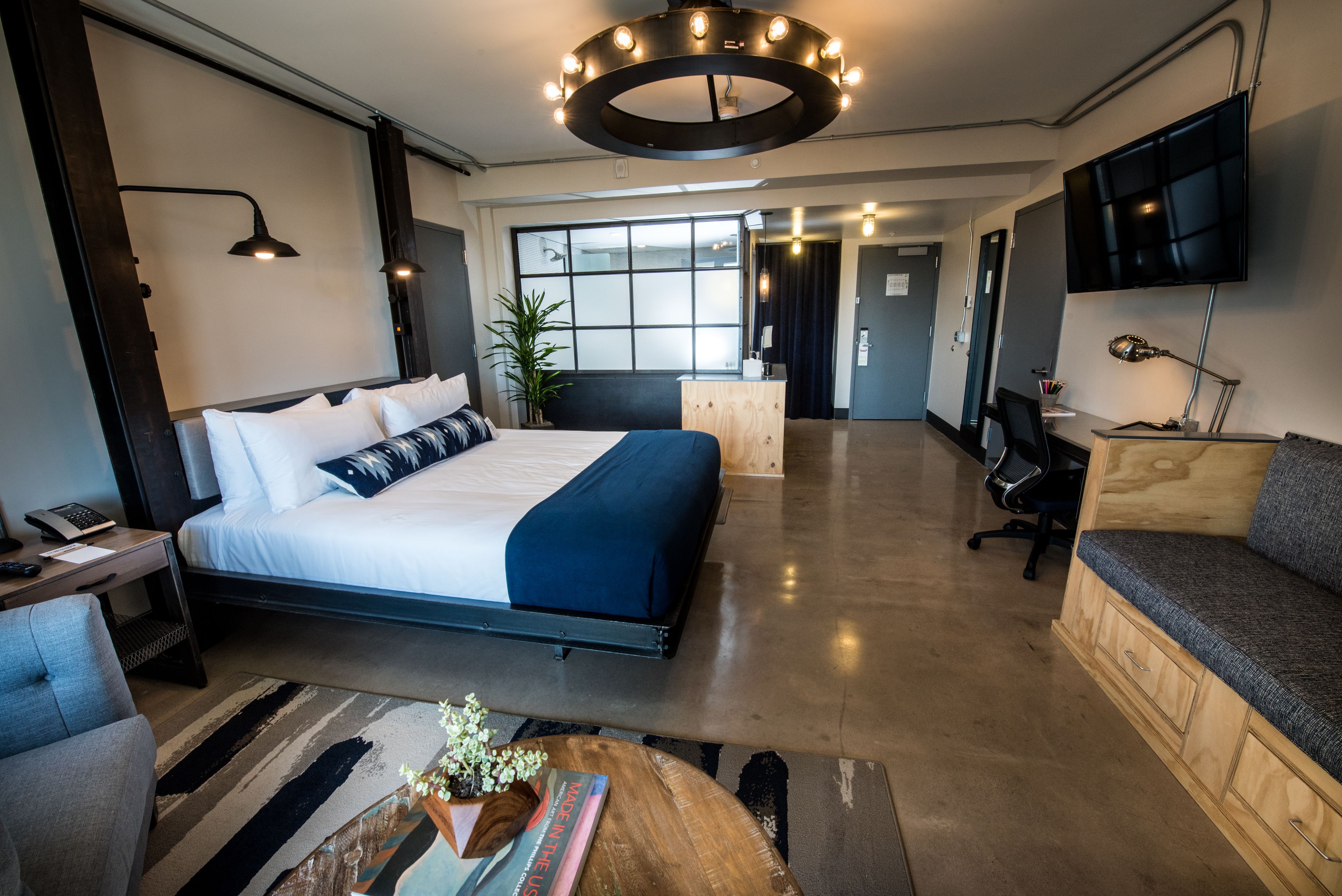 A modern hotel room with a large bed, a desk, a TV, and a sofa.
