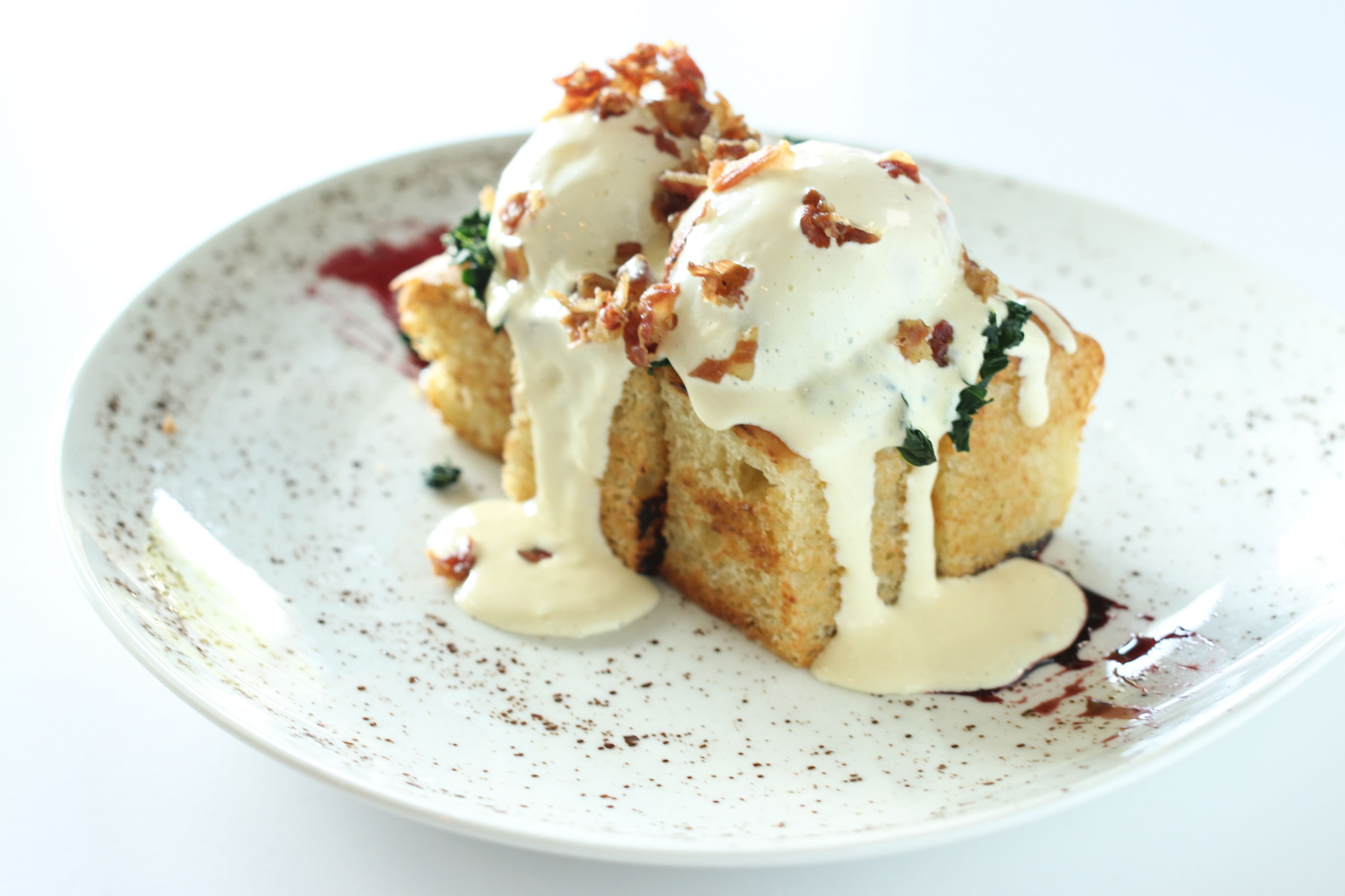 A plate with a food item topped with sauce and bacon bits.