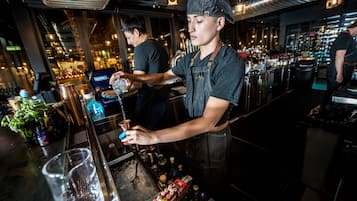 A bartender preparing a drink at a bar with a well-stocked back area and visible shelves of bottles.