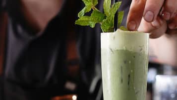 Een hoog glas met een groen drankje, versierd met muntblaadjes en een rietje, op een donker oppervlak.