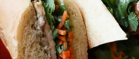 A sandwich with visible ingredients like meat, carrots, and cilantro on a red plate.