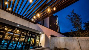 A modern building with a glass facade, outdoor seating area, and a wooden structure with lights. - FOUNDRE Phoenix (Phoenix)