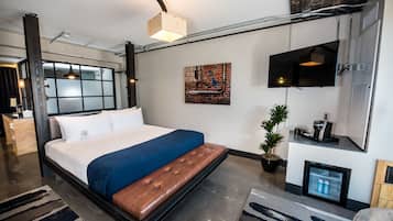 Una habitación de hotel moderna con una cama grande, un televisor de pantalla plana, un refrigerador pequeño y una planta en maceta.