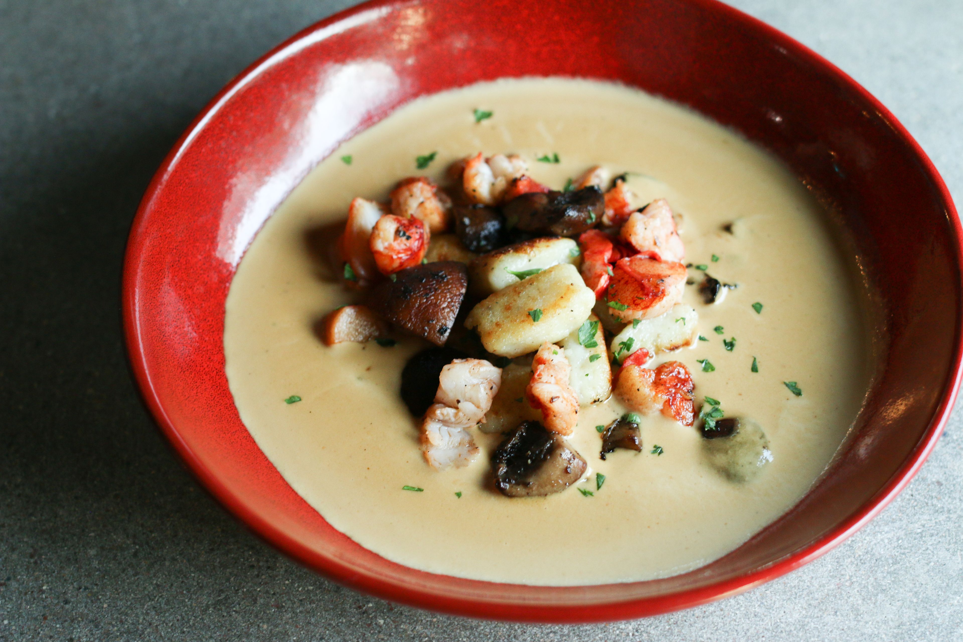 Un tazón de sopa cremosa con mariscos y verduras.
