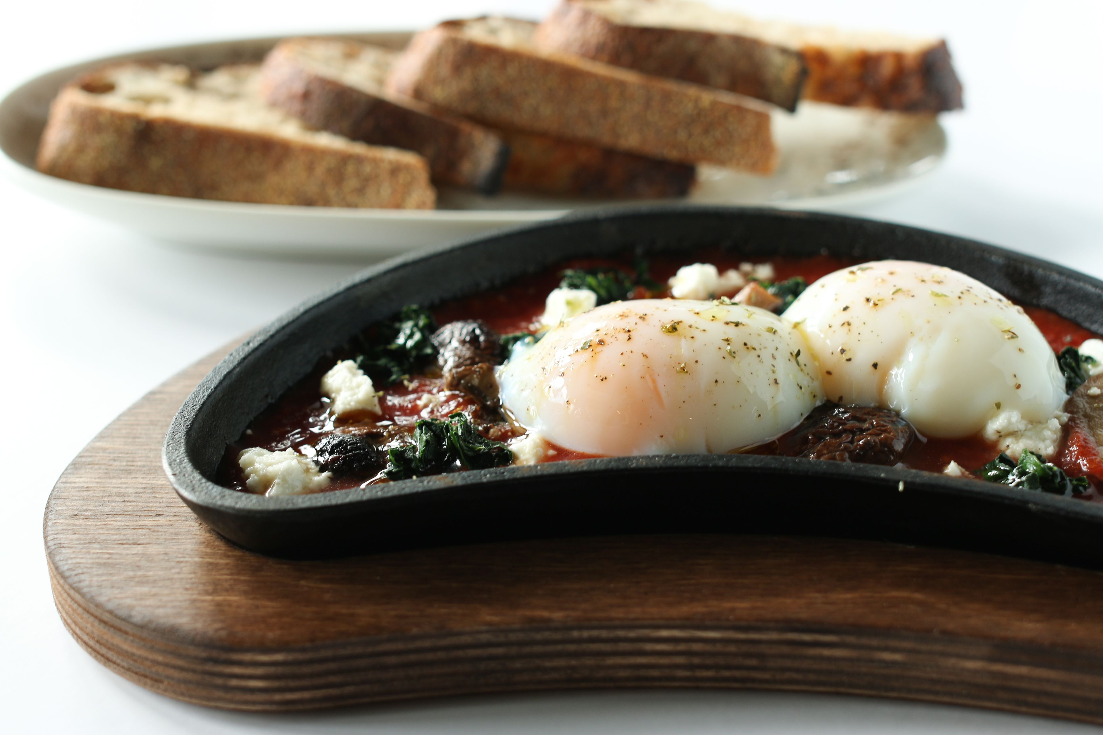 A dish with poached eggs, spinach, and feta cheese on a wooden board.