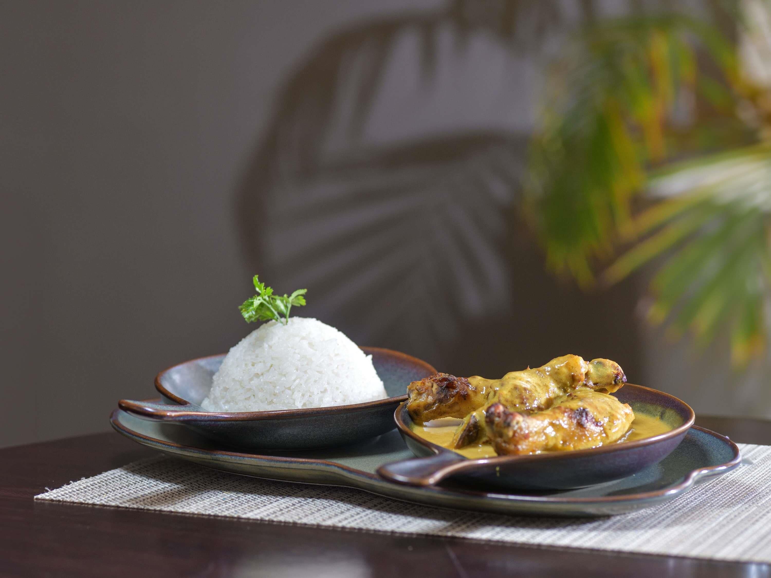 Un plato de arroz blanco adornado con una ramita de perejil, acompañado de un tazón de pollo en salsa amarilla.