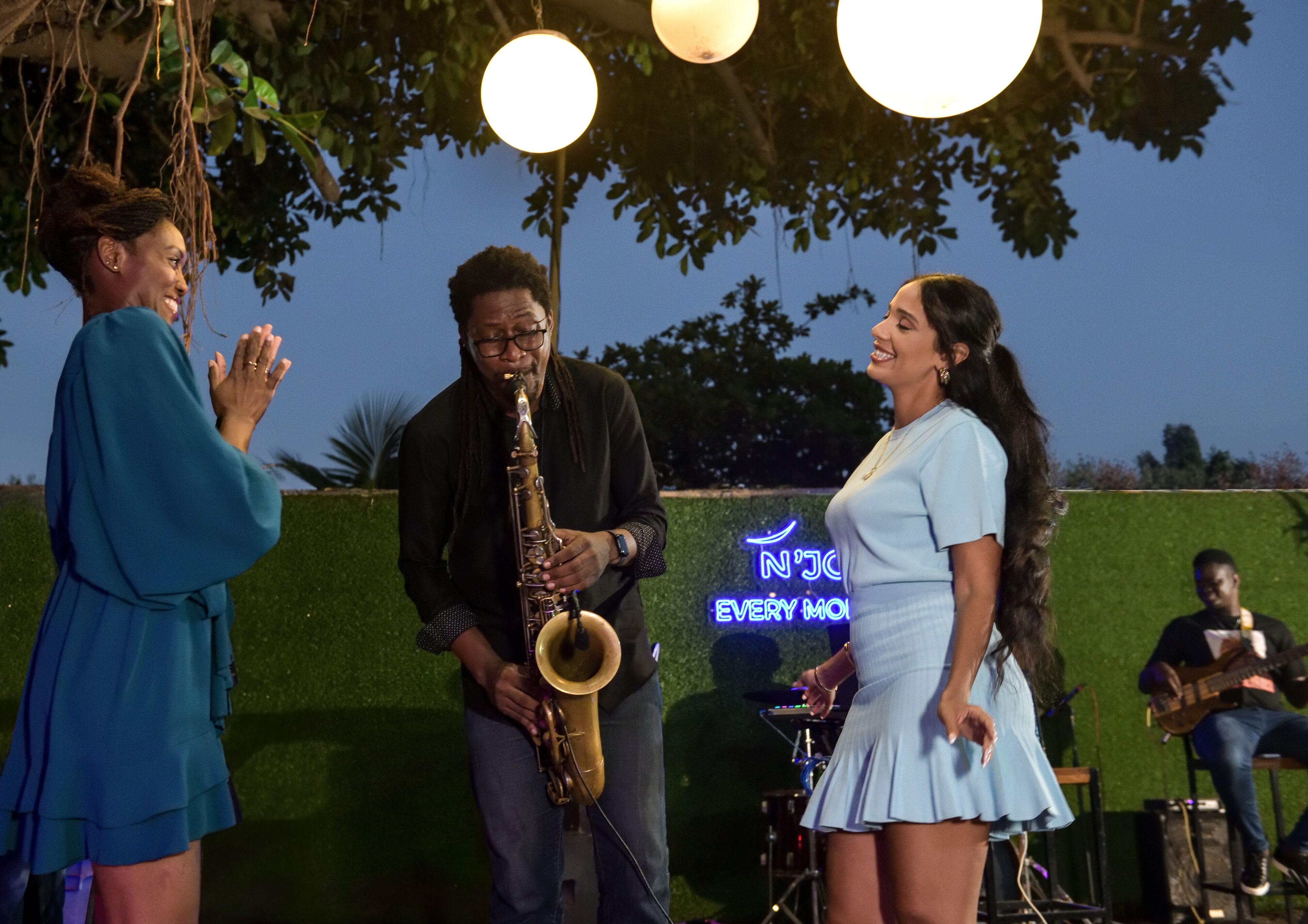 A stage with a saxophonist, a woman in a dress, and a man in a blue robe.
