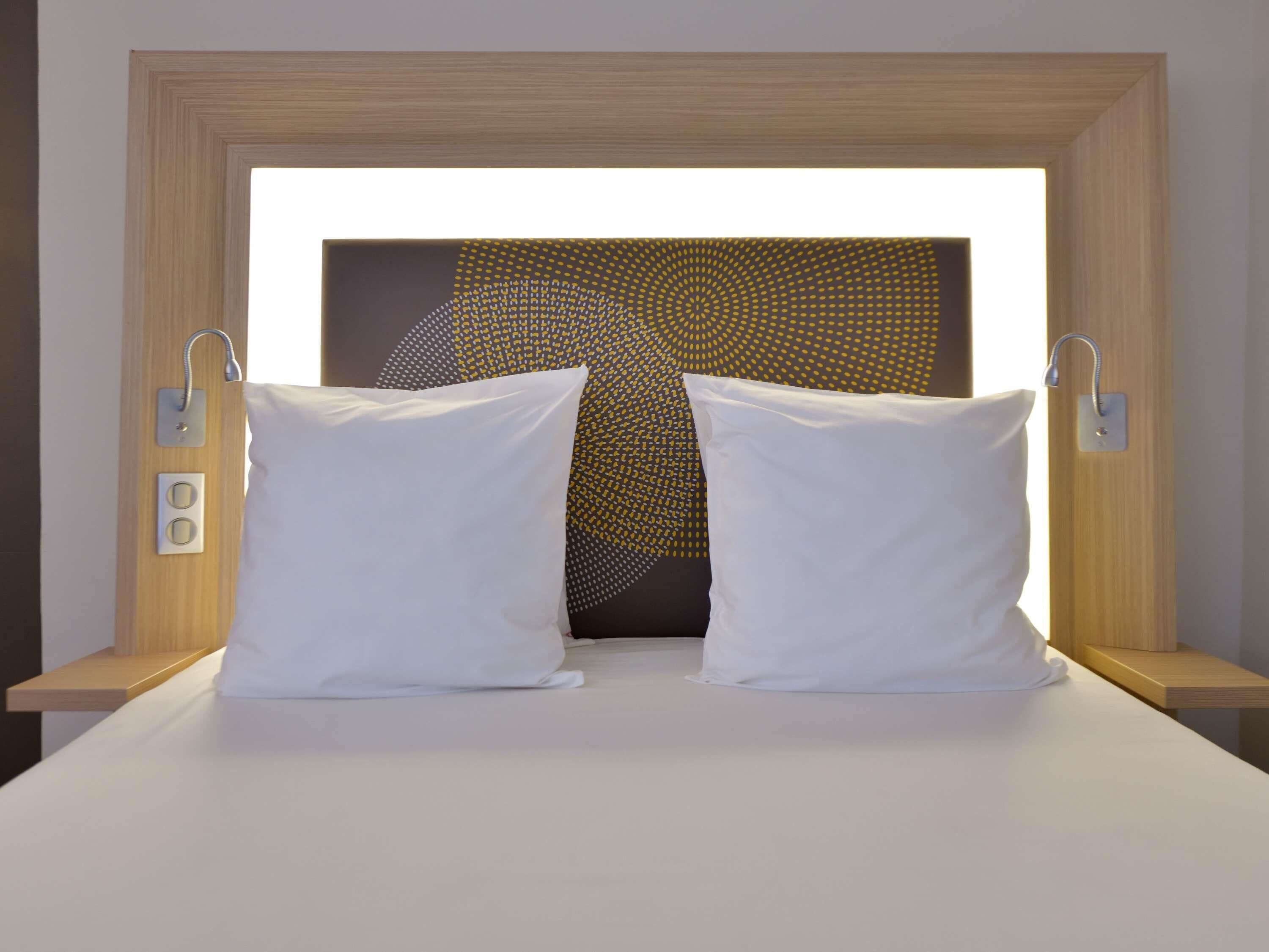 Ein Bett mit zwei weißen Kissen, einem hölzernen Kopfteil und einer Wand mit geometrischem Muster.