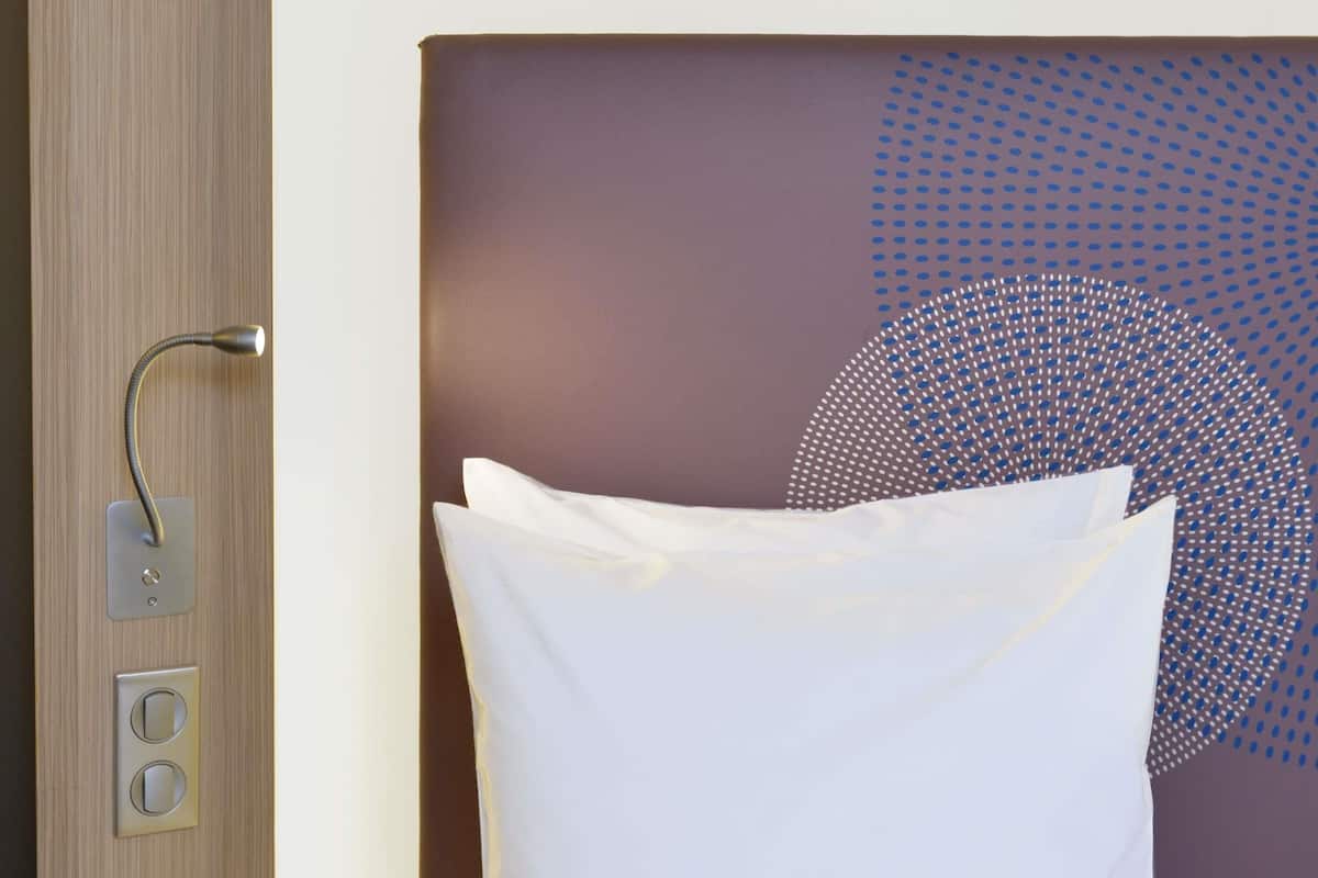 A hotel room with a bed, a wall-mounted light fixture, and a control panel with two buttons.