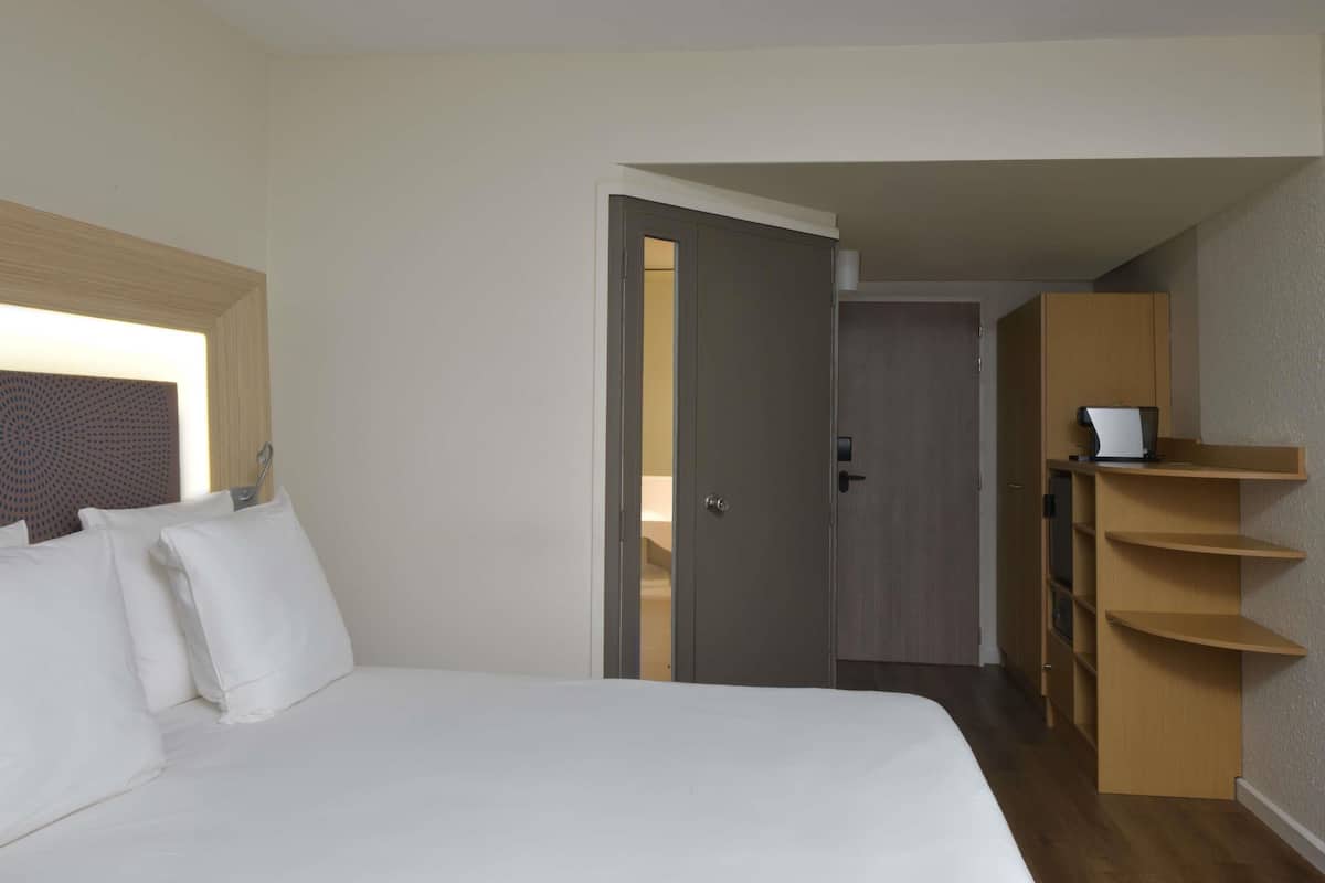 A hotel room with a large bed, a wardrobe, and a desk with a printer.