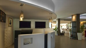 A modern reception area with a curved ceiling, a reception desk, a television, and a seating area with a plant. - Novotel Dakar (Dakar)