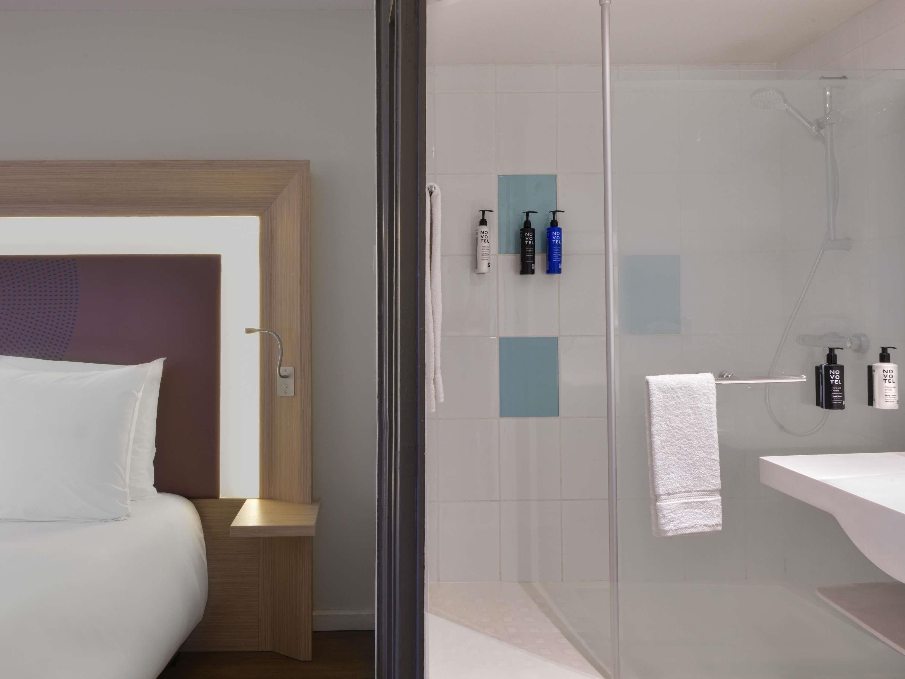 Une chambre d’hôtel avec un lit, une douche en verre et des articles de toilette fixés au mur.