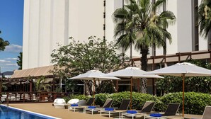 A poolside area with lounge chairs and umbrellas, a pool, and a building with vertical lines in the background. - Novotel Dakar (Dakar)