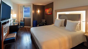 A hotel room with a bed, a desk with a chair, a TV, a window with curtains, a lamp, and a painting on the wall. - Novotel Dakar (Dakar)