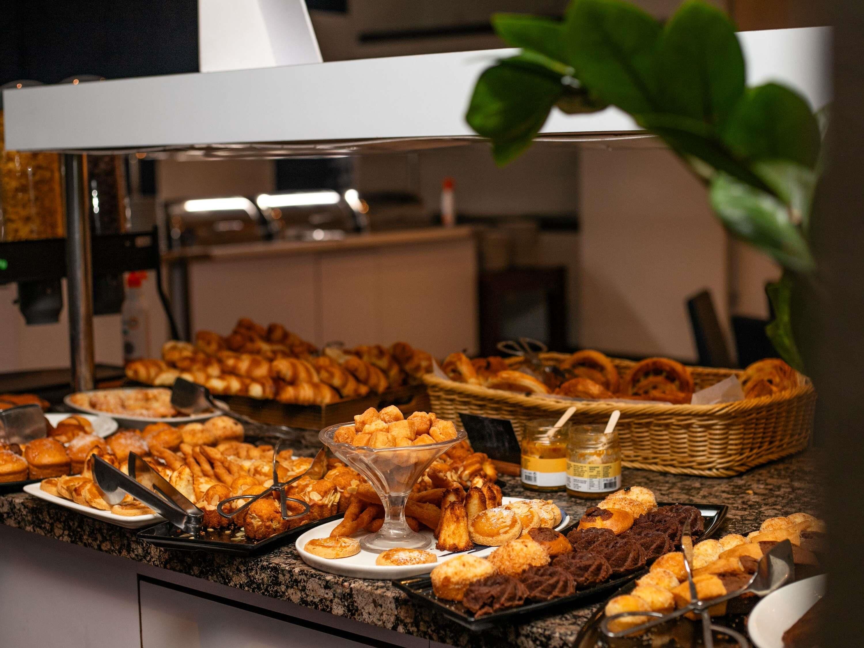 A buffet with various pastries and bread, including croissants and muffins, arranged on a counter.