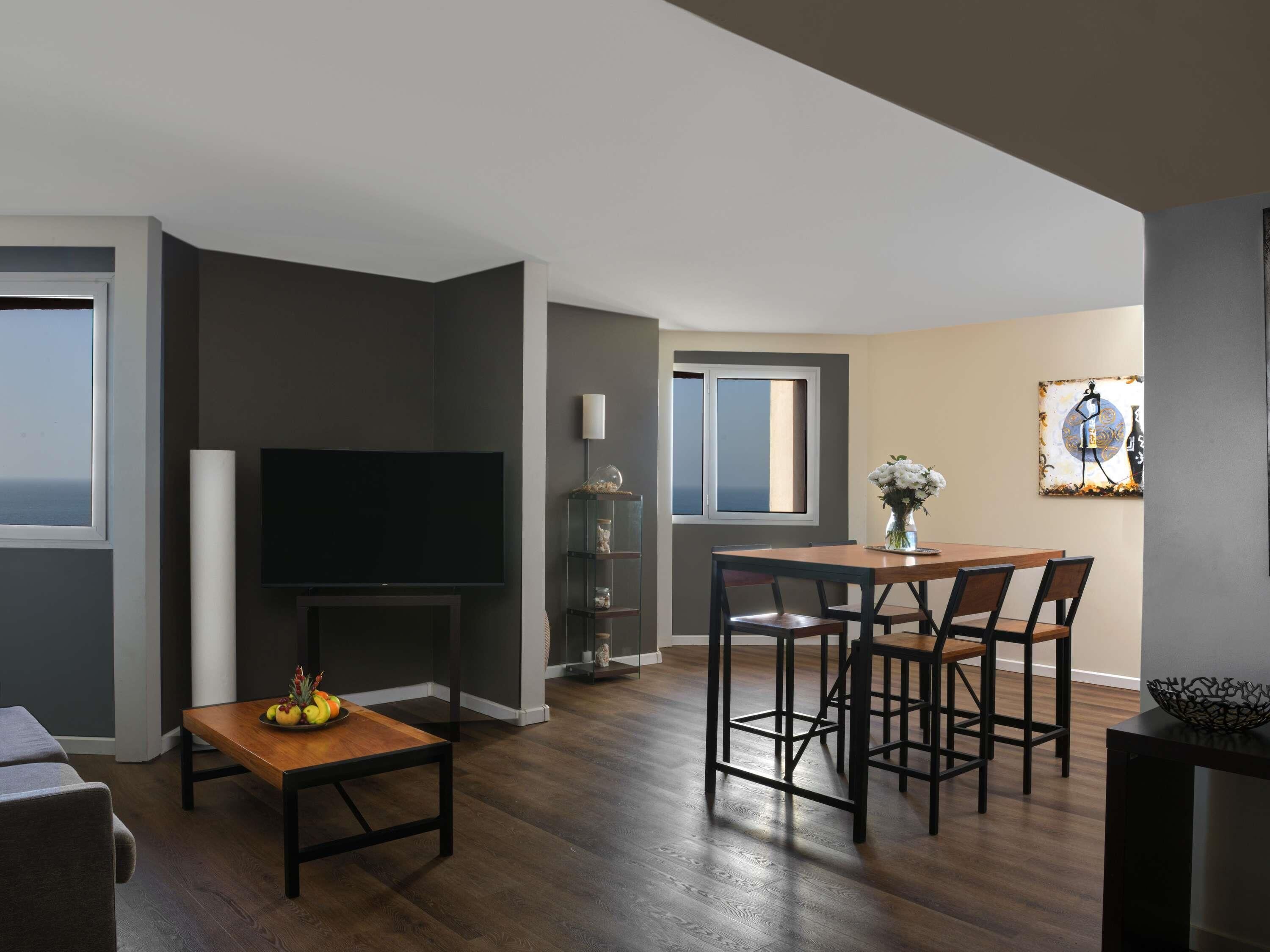A modern living room with a flat-screen TV, a dining area with a wooden table and chairs, and a fireplace.
