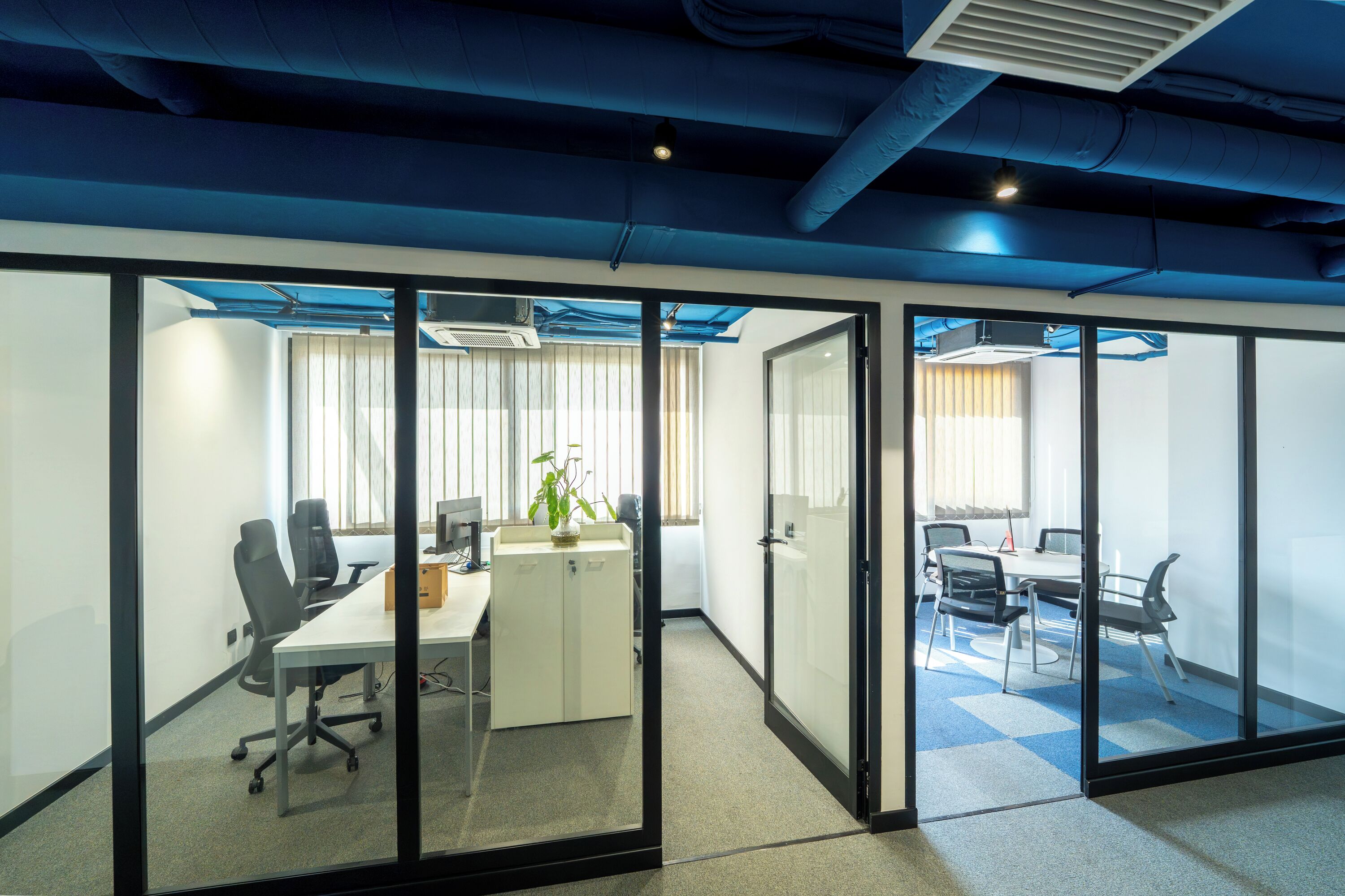 A modern office space with glass partitions, a meeting table, and office chairs.