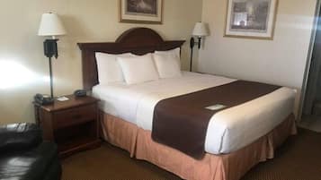 Una habitación de hotel con una cama grande, dos lámparas de noche, una mesita de noche, un sillón de cuero y dos cuadros en la pared.