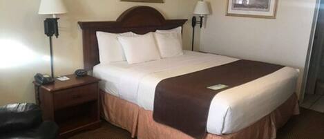 Una habitación de hotel con una cama grande, dos lámparas de noche, una mesita de noche, un sillón de cuero y dos cuadros en la pared.