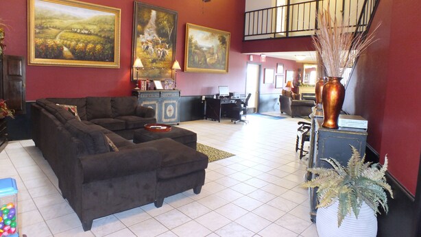 A spacious living area with a sectional sofa, a coffee table, and a fireplace. There are two large paintings on the wall, a ceiling fan, and a staircase leading to an upper level. - Days Inn by Wyndham Abilene (Abilene)
