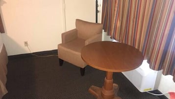 Una habitación pequeña con un sillón beige, una mesa redonda de madera, una lámpara y una cortina a rayas.