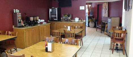 A dining area with wooden tables and chairs, a refrigerator, and a coffee station.