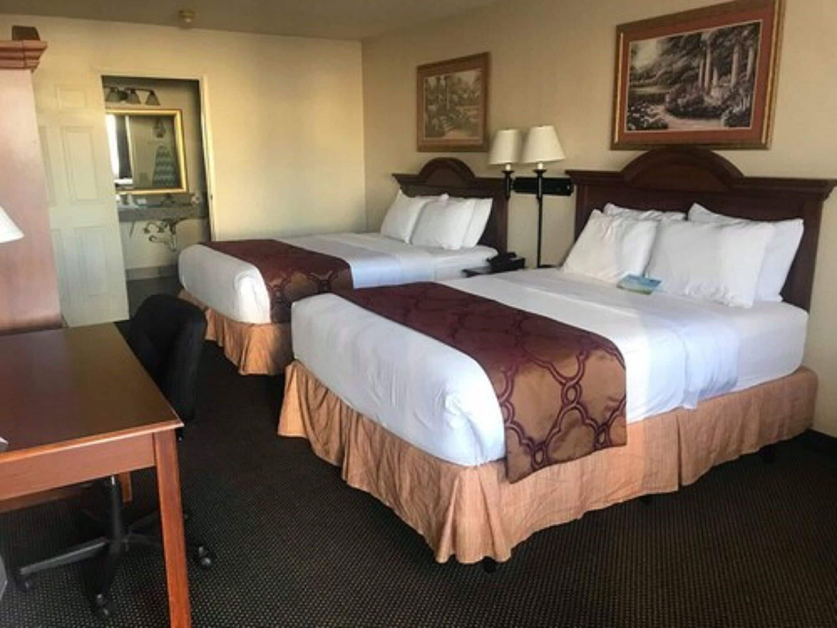 Une chambre d’hôtel avec deux lits, un bureau, une chaise et un miroir.