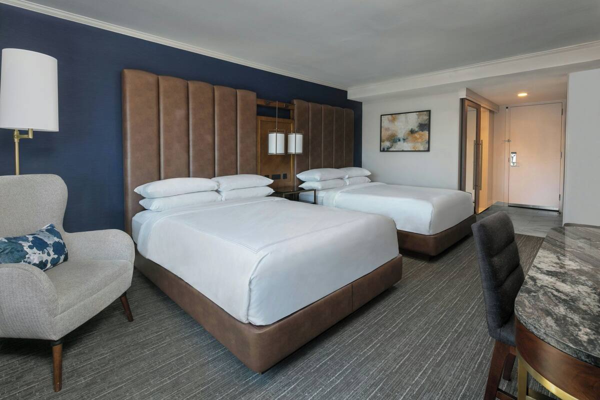 A hotel room with two beds, a sofa, a dining table, and a painting on the wall.