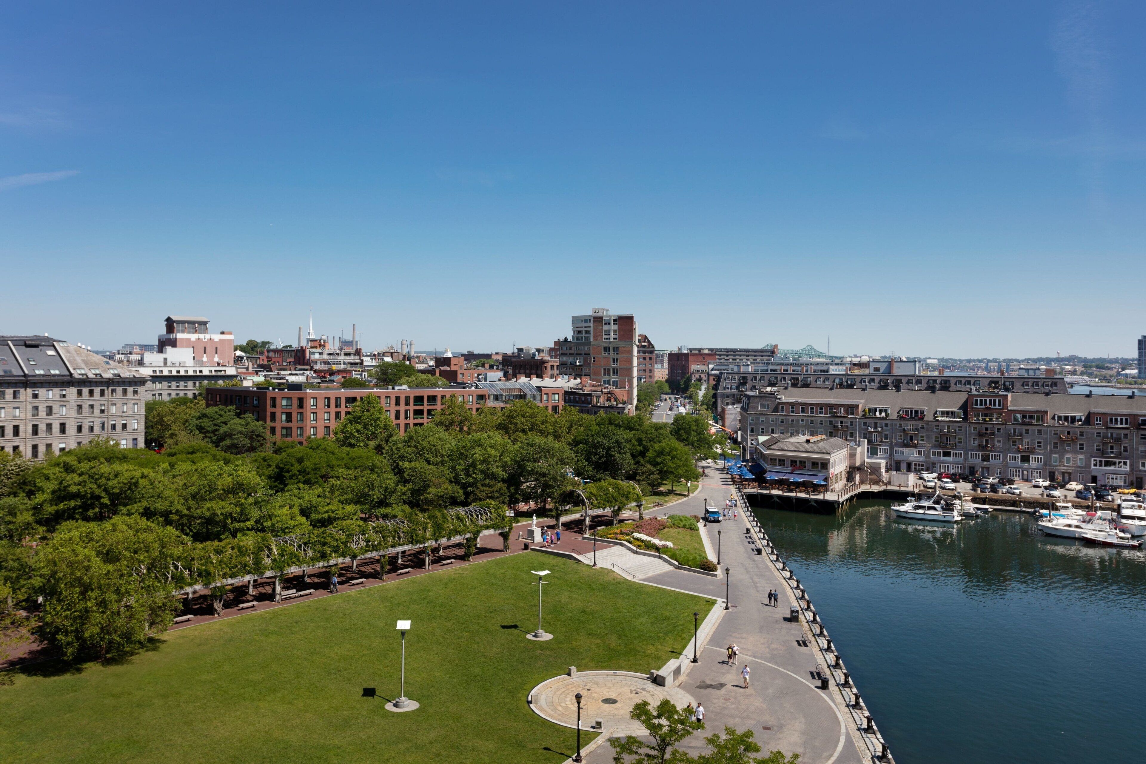 Une vue sur la ville, avec ses bâtiments, un parc et un port de plaisance, prise depuis les rives d’une rivière.