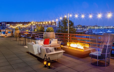 A rooftop terrace with outdoor seating, a fire feature, and string lights.