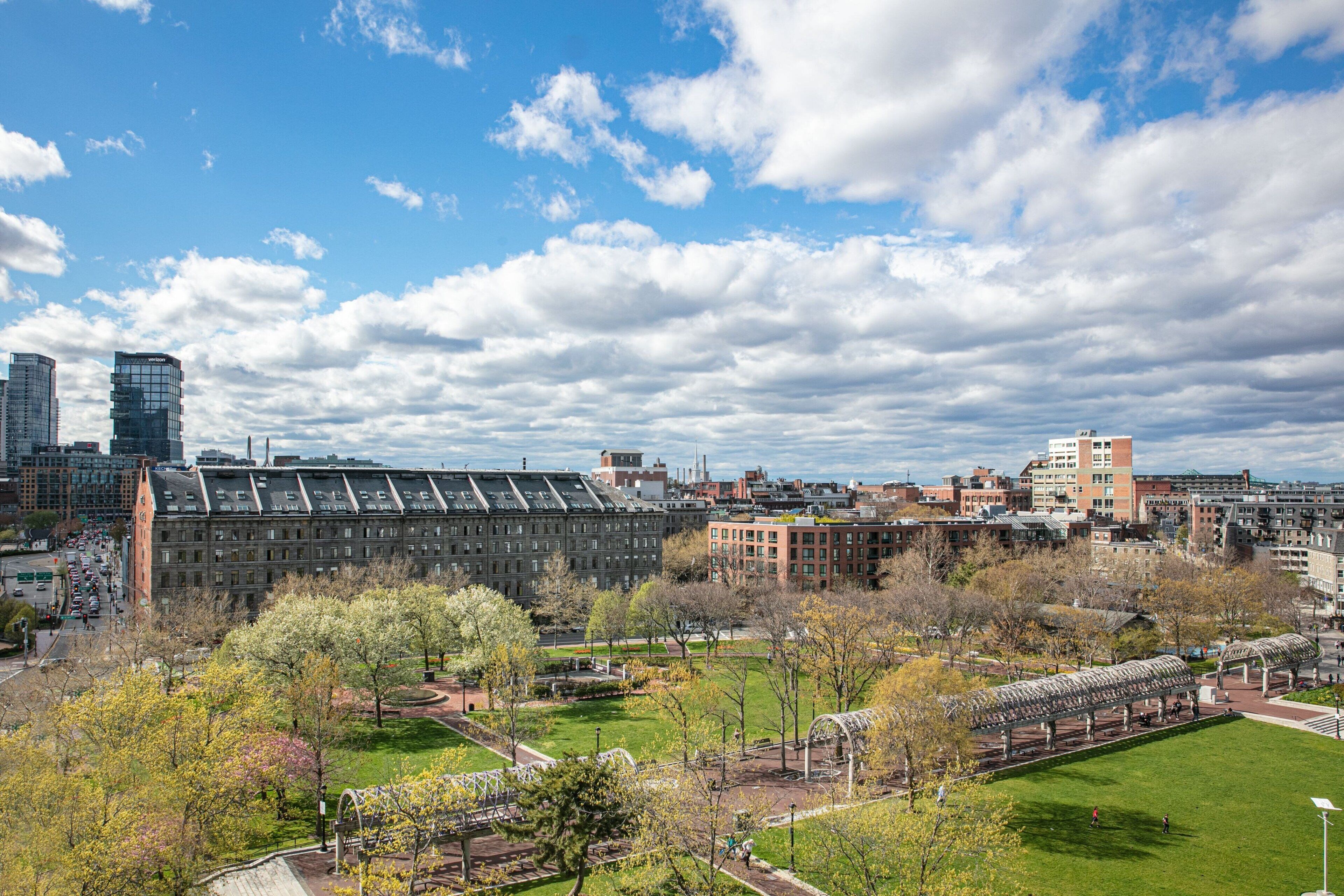 A cityscape with a large building complex, green spaces, and a clear sky.
