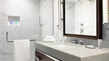 A modern bathroom with a marble-tiled wall, a large mirror, a sink with a soap dispenser, and a towel rack.
