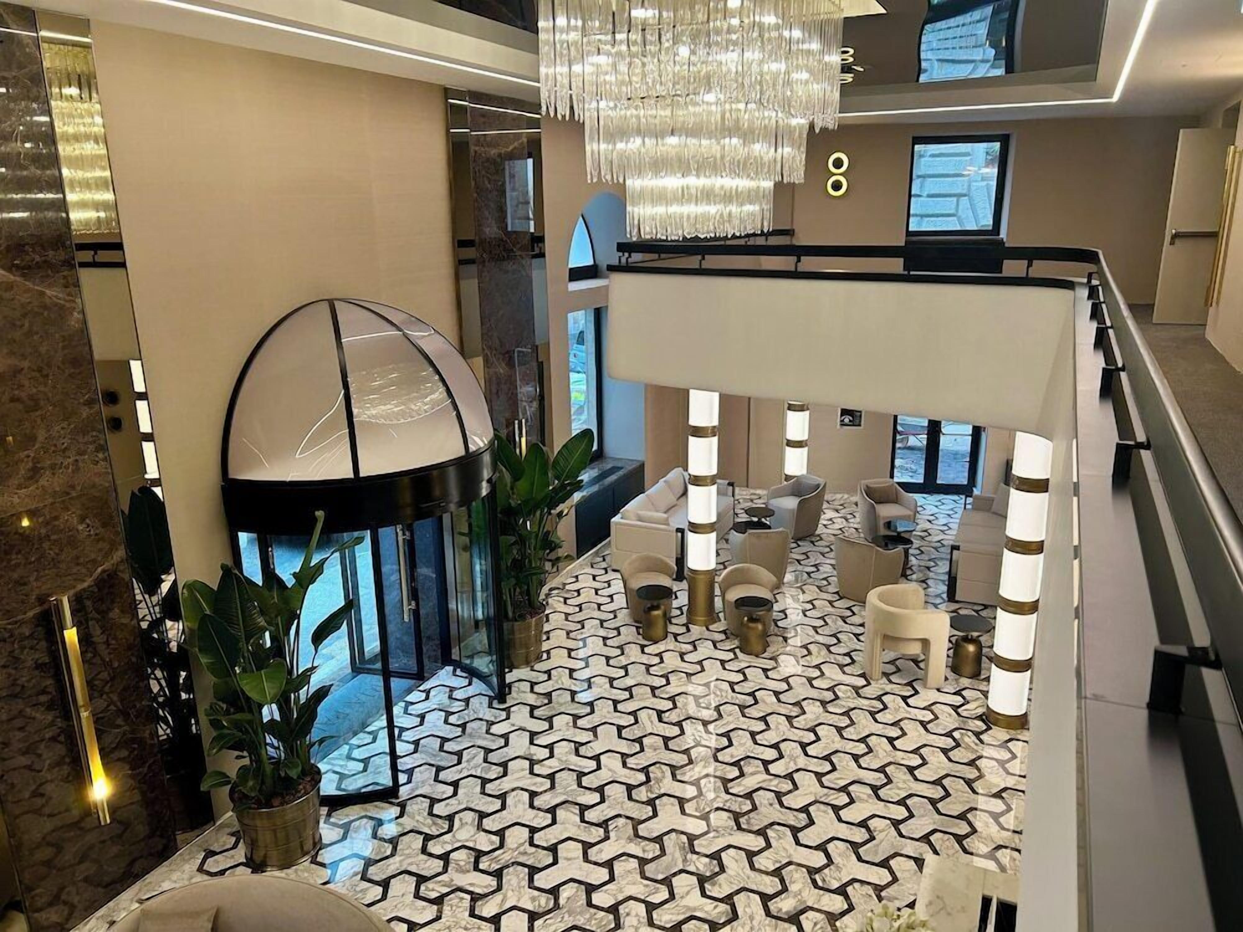 A modern hotel lobby with a patterned floor, seating area, and a large chandelier.