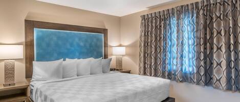 Habitación de hotel con una cama grande, dos mesitas de noche, cabecera y cortina estampada.