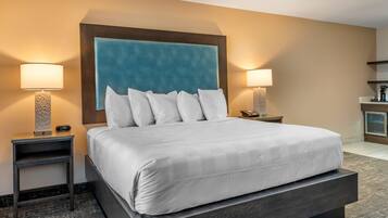 Habitación de hotel con una cama grande, dos mesitas de noche con lámparas, una mesita auxiliar, un escritorio pequeño y una estantería empotrada.