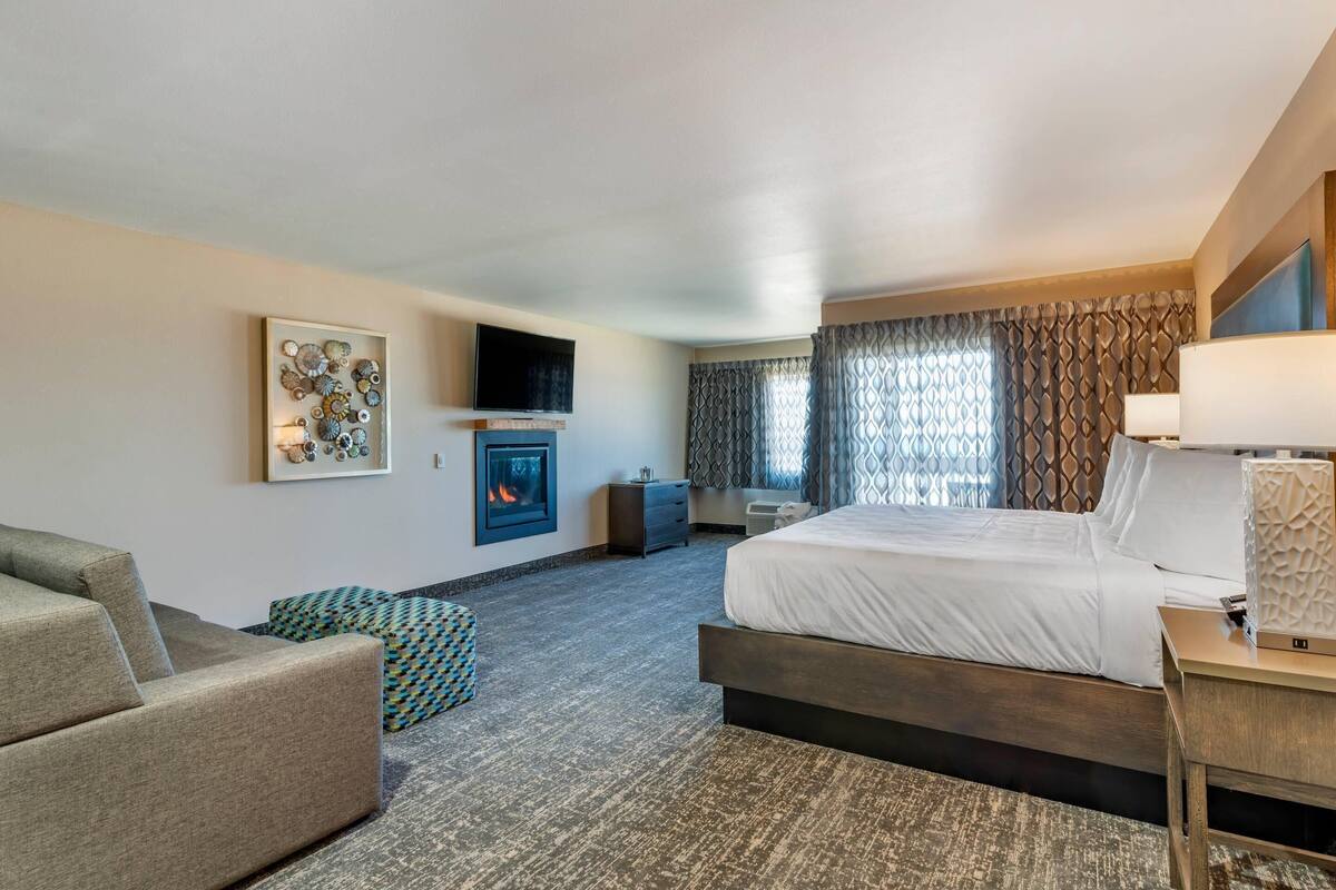 Una habitación de hotel con cama, sofá, televisión, chimenea y ventana con cortinas.