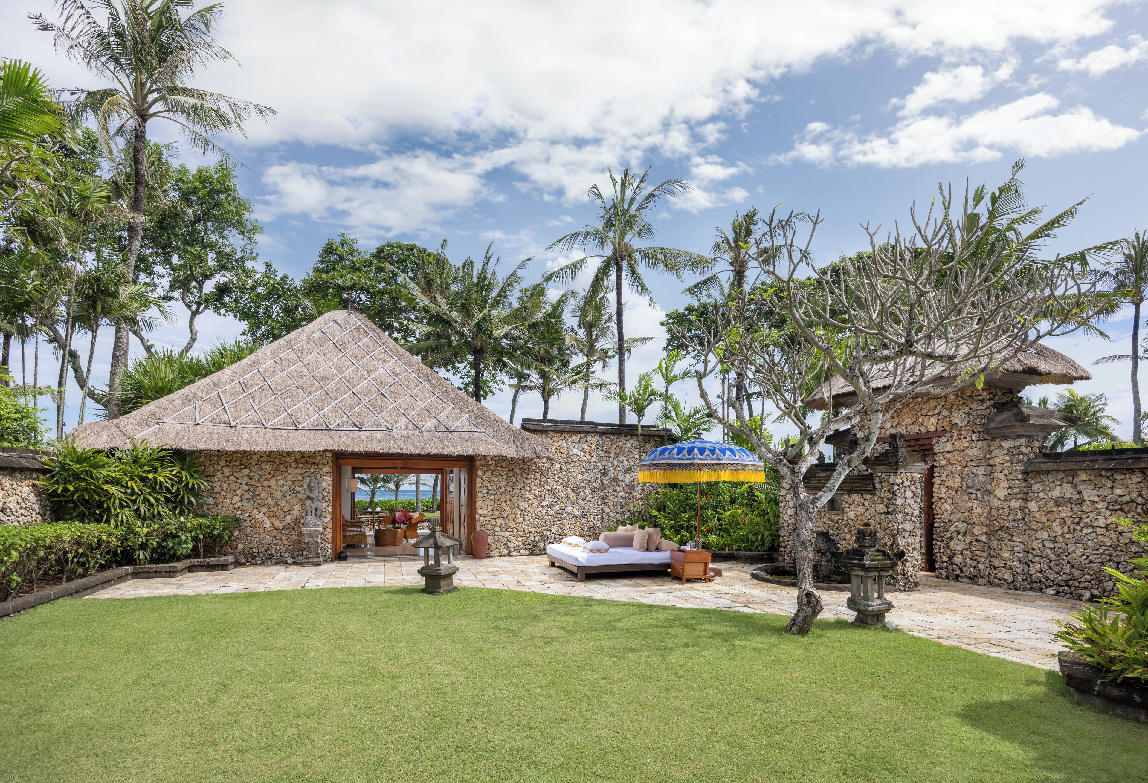 A stone building with a thatched roof, a patio with a sofa, and a lawn.