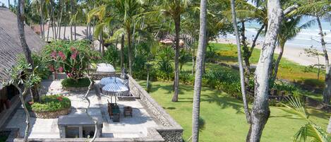 A stone building with a patio, surrounded by palm trees and a beach view.