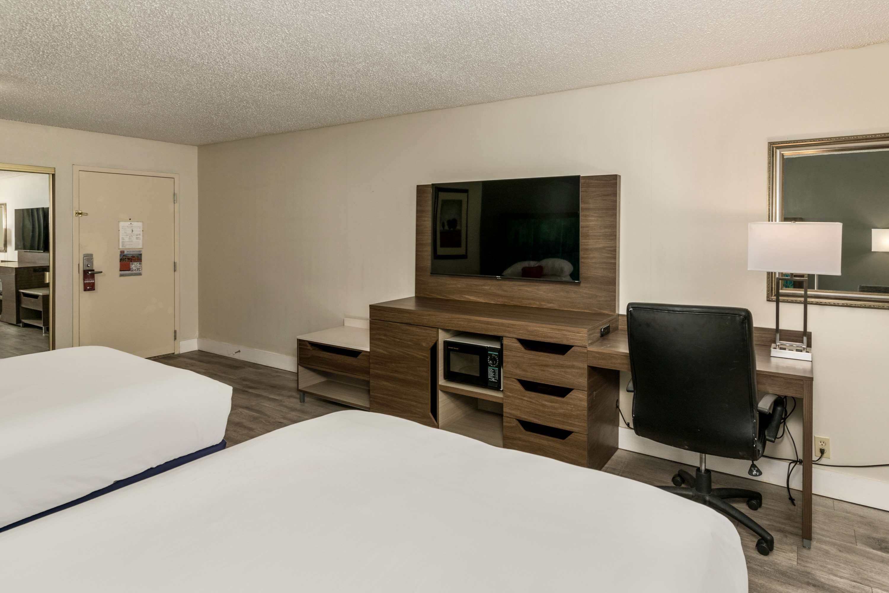 Une chambre d’hôtel avec deux lits, un bureau en bois avec un ordinateur, une chaise, un four à micro-ondes et un grand miroir.