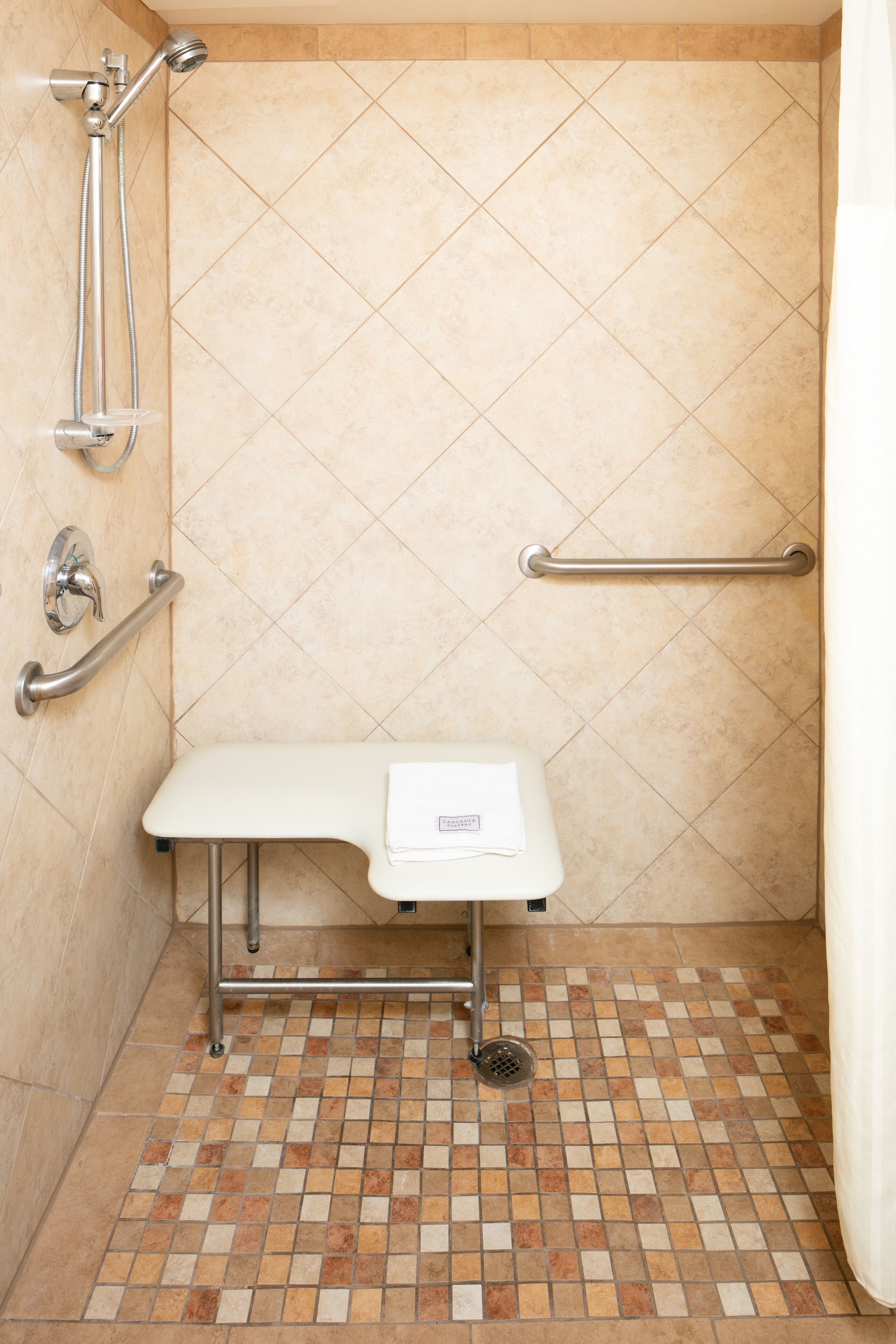 Zona de ducha con barra de apoyo, un banco y cabezal de ducha manual.