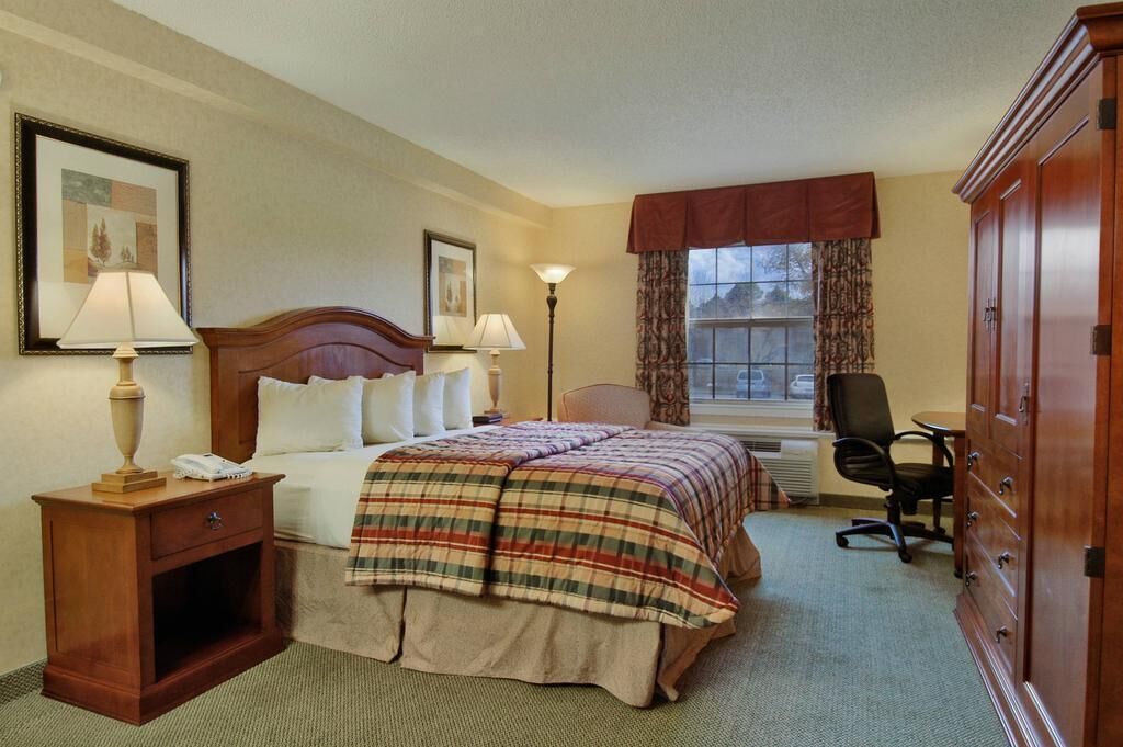 Une chambre d’hôtel comprenant un lit, des lampes de chevet, un bureau avec une chaise, une armoire et une fenêtre avec des rideaux.