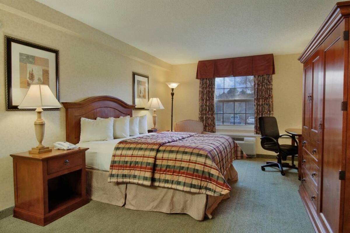A hotel room with a bed, bedside lamps, a desk with a chair, a wardrobe, and a window with curtains.