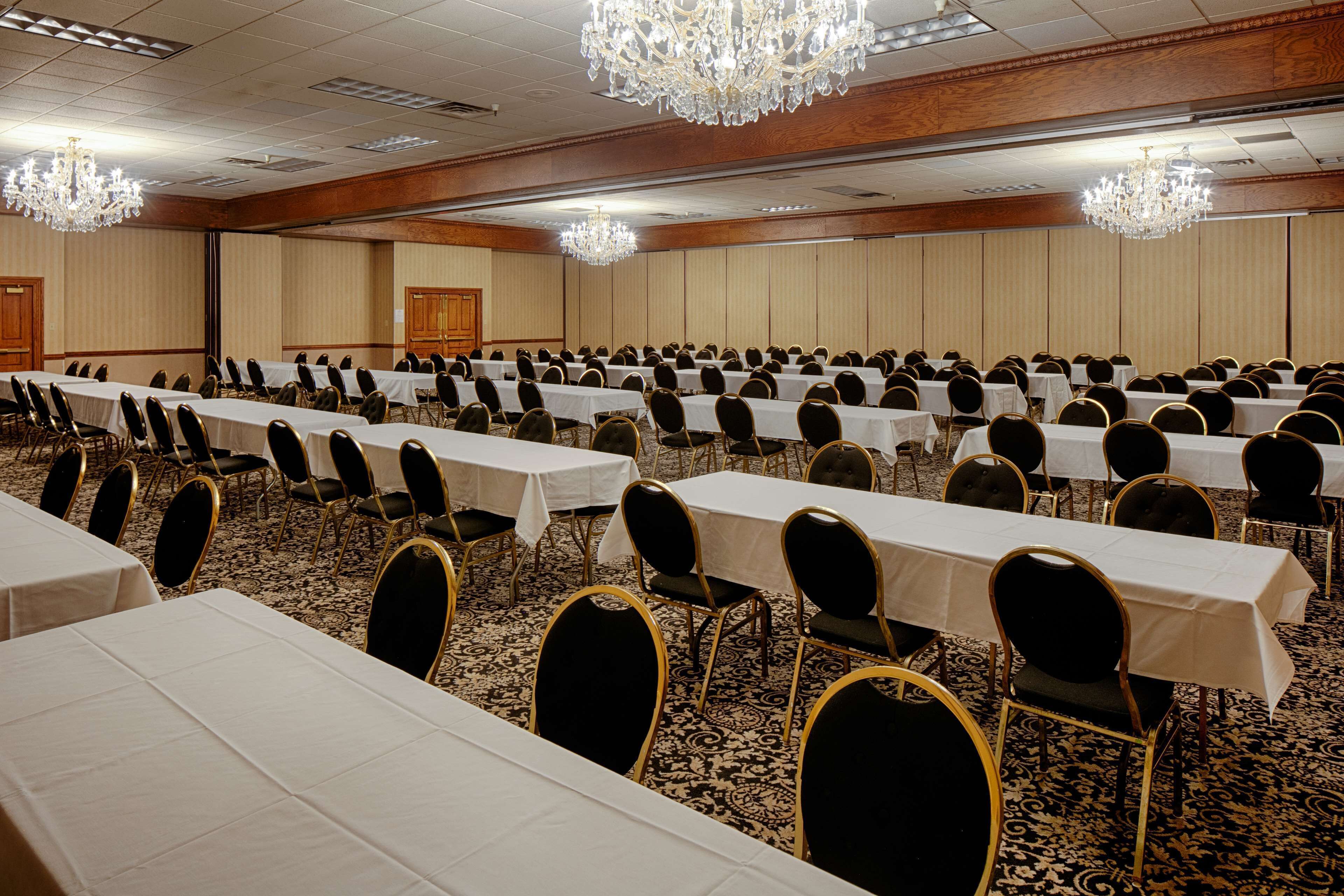Une salle de conférence avec des rangées de tables et de chaises, des lustres et un sol recouvert de moquette.