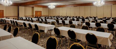 Une salle de conférence avec des rangées de tables et de chaises, des lustres et un sol recouvert de moquette.