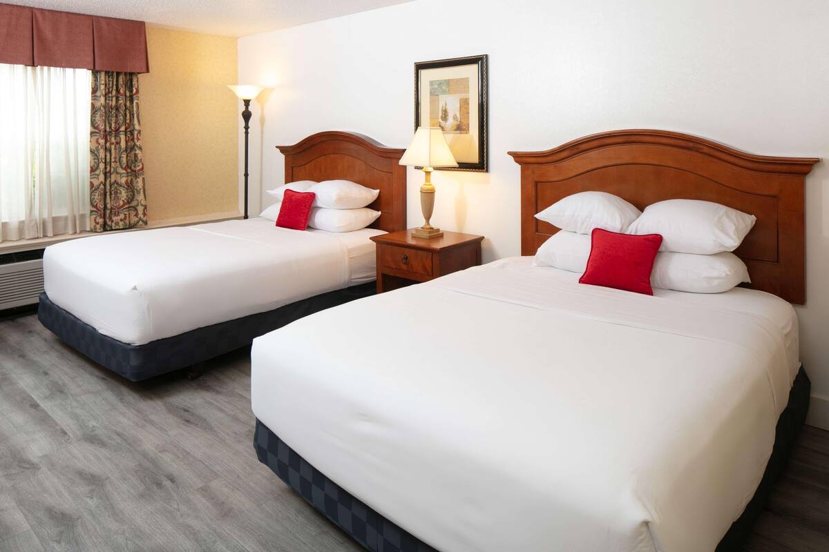Two single beds with wooden headboards, a bedside table with a lamp, and a window with curtains.