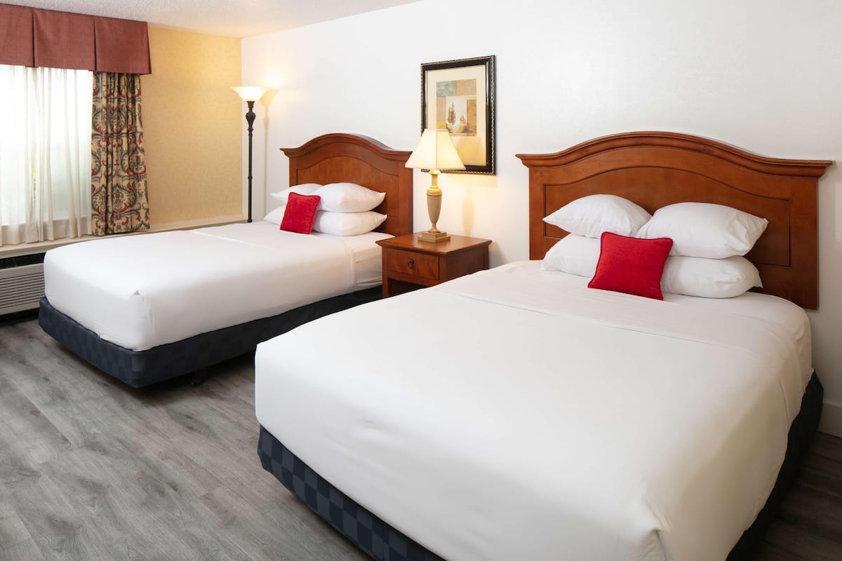 Two single beds with wooden headboards, a bedside table with a lamp, and a window with curtains.